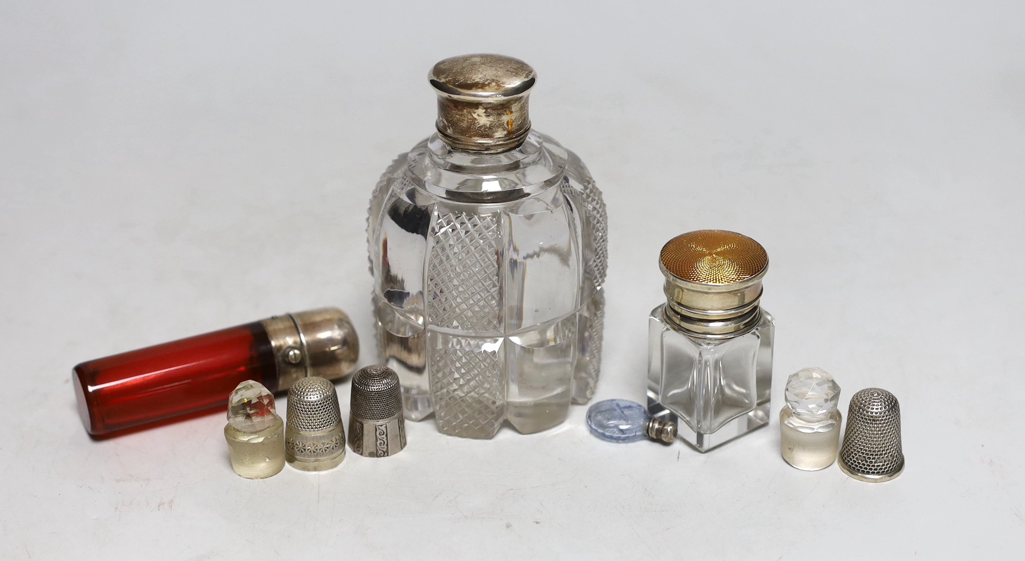 Three silver or white metal mounted glass scent bottles including enamelled, 56mm and ruby glass, one other, two glass stoppers and three thimbles.